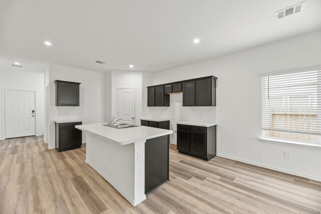 kitchen featuring visible vents, a center island with sink, light wood-style flooring, and a sink