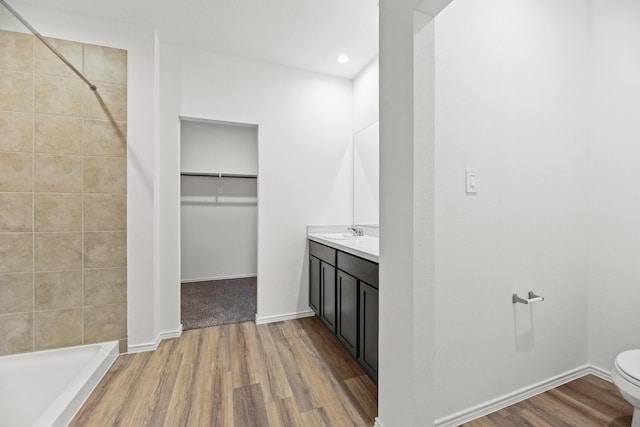 bathroom with wood finished floors, toilet, vanity, and tiled shower
