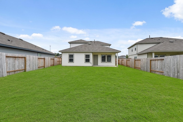 rear view of house featuring roof with shingles, a yard, and a fenced backyard