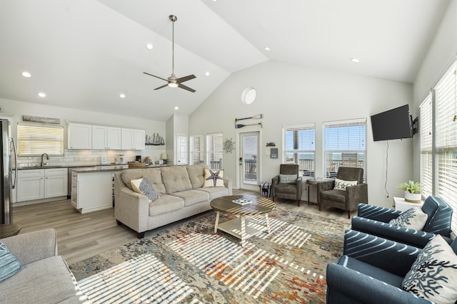 living room with light hardwood / wood-style floors, high vaulted ceiling, ceiling fan, and sink