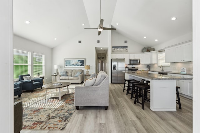 living room featuring light hardwood / wood-style floors, high vaulted ceiling, ceiling fan, and sink