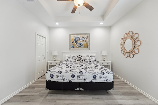 bedroom with a tray ceiling, ceiling fan, and light hardwood / wood-style flooring