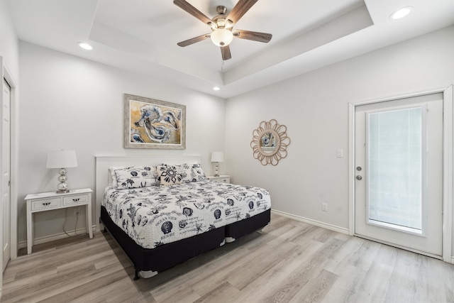 bedroom with ceiling fan, light hardwood / wood-style floors, access to outside, and a tray ceiling