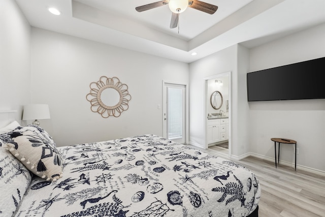 bedroom featuring ceiling fan, light wood-type flooring, a tray ceiling, and ensuite bath