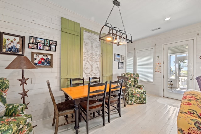 dining area featuring light wood-type flooring, wood walls, and a notable chandelier