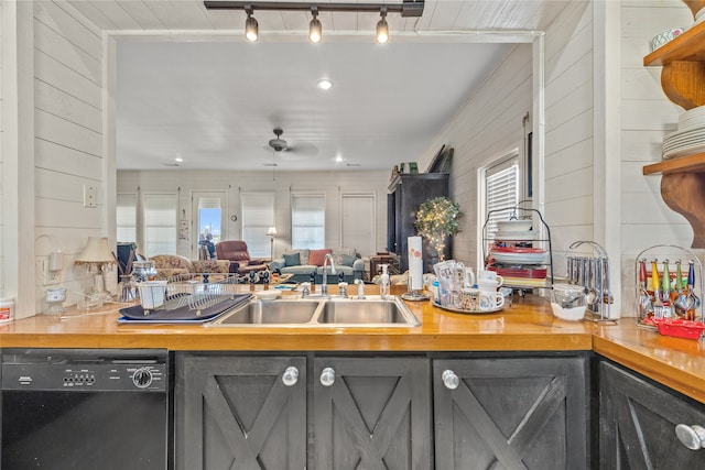 kitchen with ceiling fan, wood walls, sink, track lighting, and dishwasher