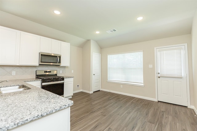 kitchen with light stone countertops, stainless steel appliances, sink, white cabinetry, and lofted ceiling