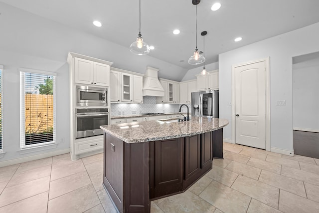 kitchen with custom exhaust hood, lofted ceiling, sink, an island with sink, and stainless steel appliances