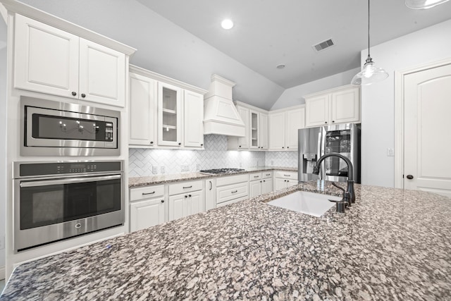 kitchen with sink, vaulted ceiling, white cabinets, custom range hood, and appliances with stainless steel finishes