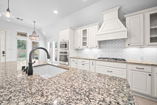 kitchen with lofted ceiling, sink, custom range hood, appliances with stainless steel finishes, and white cabinetry