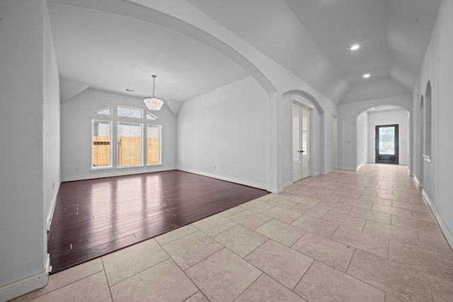 unfurnished living room with light hardwood / wood-style flooring, vaulted ceiling, and an inviting chandelier