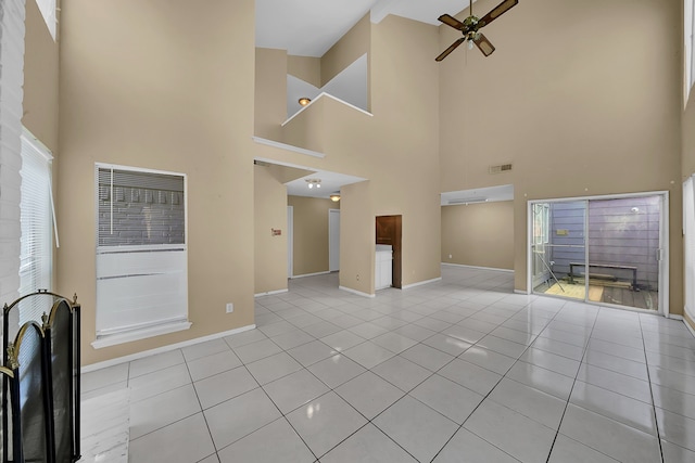 unfurnished living room with a high ceiling, ceiling fan, a fireplace, and light tile patterned floors