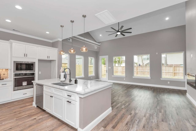 kitchen with light stone counters, a kitchen island with sink, sink, appliances with stainless steel finishes, and ceiling fan