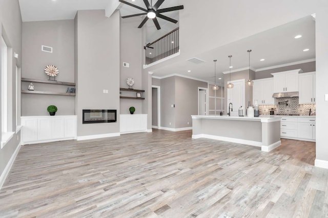 unfurnished living room featuring light hardwood / wood-style floors, ornamental molding, a towering ceiling, and ceiling fan