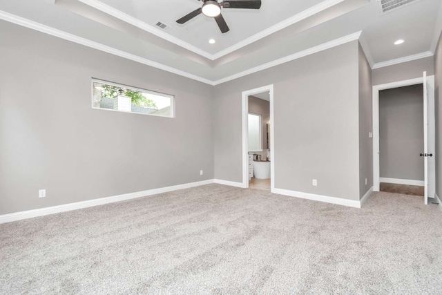 unfurnished bedroom with a tray ceiling, light colored carpet, ensuite bath, ornamental molding, and ceiling fan