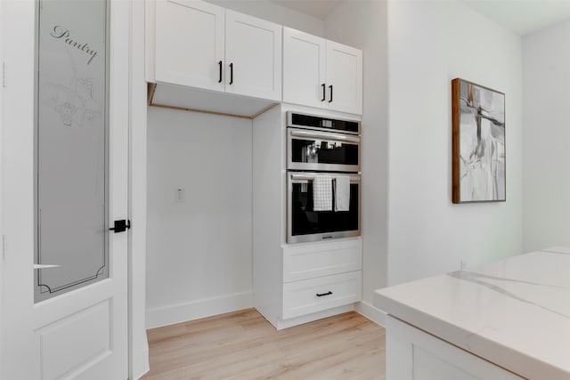 kitchen with white cabinets, stainless steel double oven, light hardwood / wood-style floors, and light stone countertops