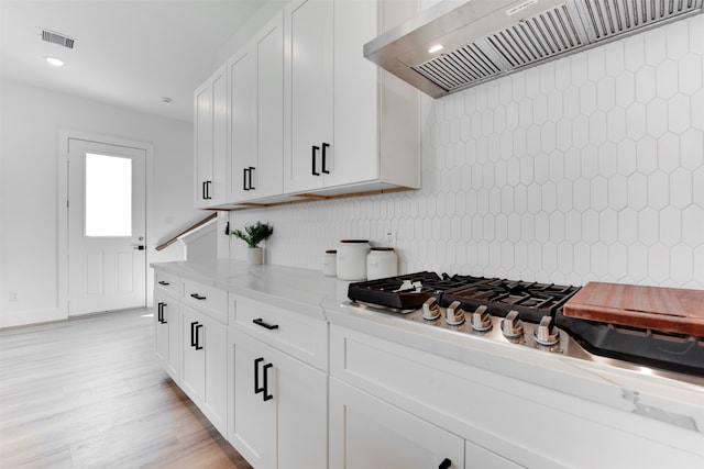 kitchen featuring white cabinets, custom range hood, light wood-type flooring, and light stone counters