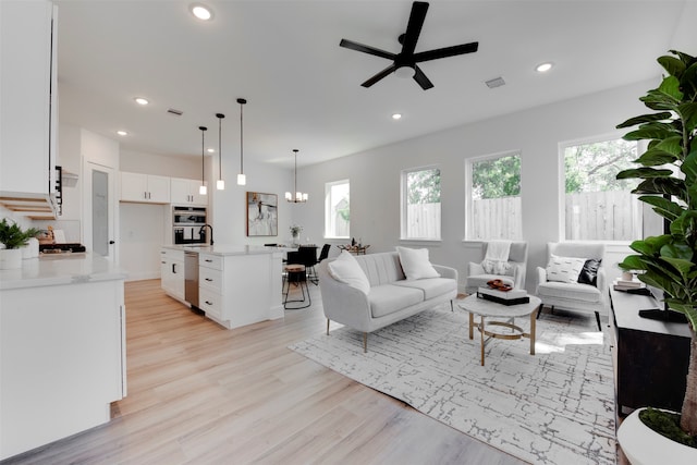 living room with a wealth of natural light, light hardwood / wood-style flooring, and ceiling fan with notable chandelier