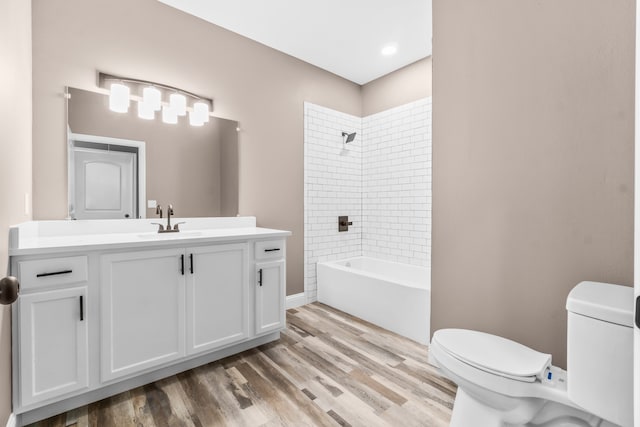 full bathroom with hardwood / wood-style floors, tiled shower / bath, vanity, and toilet