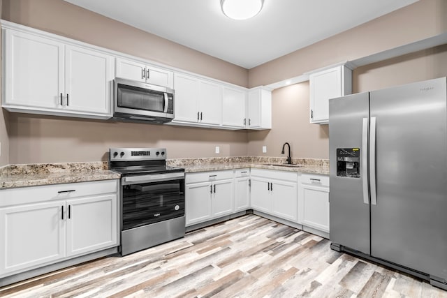 kitchen with stainless steel appliances, white cabinets, light wood-type flooring, and sink