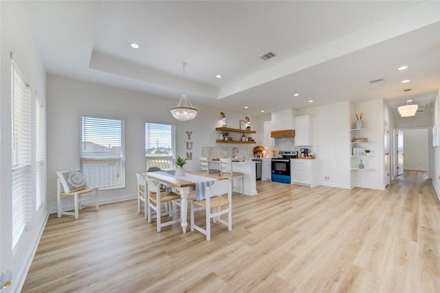 dining room with a tray ceiling and light hardwood / wood-style flooring