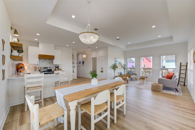 dining space with sink, light wood-type flooring, a chandelier, and a raised ceiling