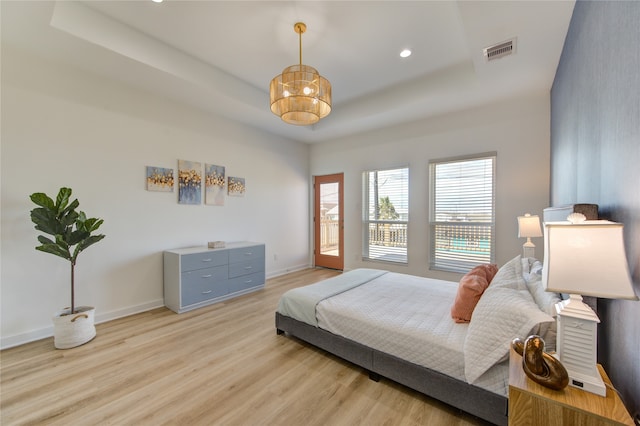 bedroom with a notable chandelier, a tray ceiling, and light hardwood / wood-style floors