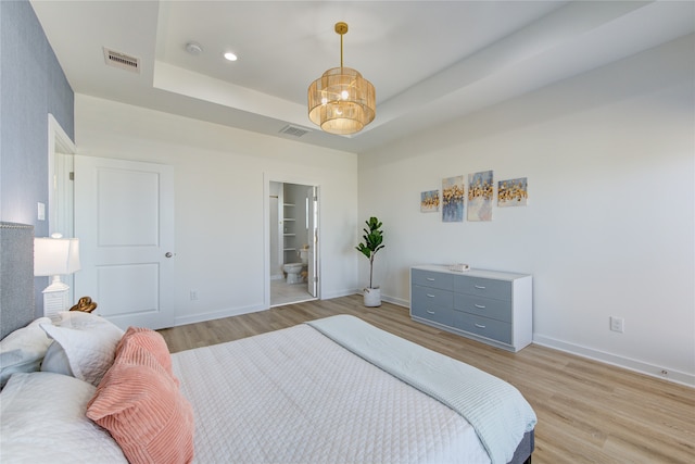 bedroom with ensuite bath, light hardwood / wood-style floors, a raised ceiling, and a chandelier