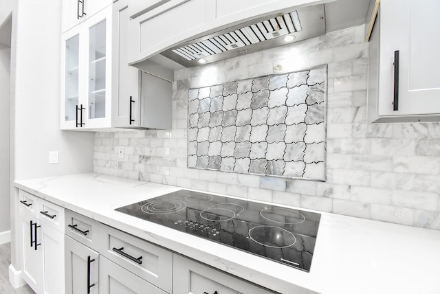 kitchen with black electric stovetop, white cabinets, light stone counters, and ventilation hood