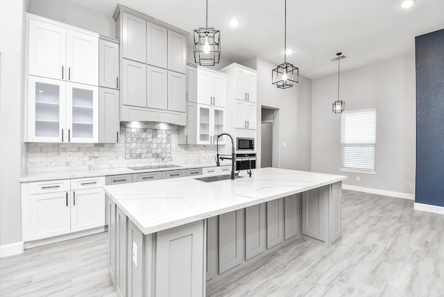 kitchen featuring light stone countertops, sink, a kitchen island with sink, and hanging light fixtures