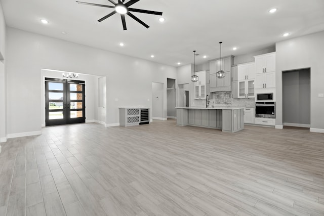 unfurnished living room with ceiling fan, a towering ceiling, light hardwood / wood-style floors, french doors, and sink