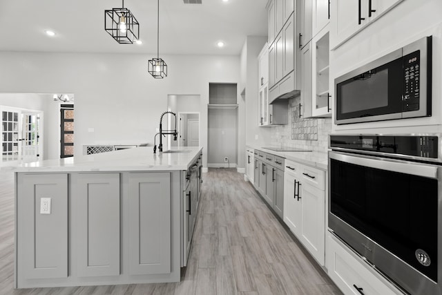 kitchen with an island with sink, hanging light fixtures, sink, light stone countertops, and appliances with stainless steel finishes