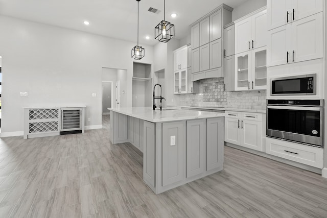 kitchen with stainless steel appliances, a center island with sink, sink, and light wood-type flooring