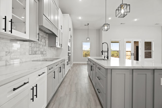 kitchen featuring pendant lighting, black electric cooktop, a center island with sink, and white cabinets