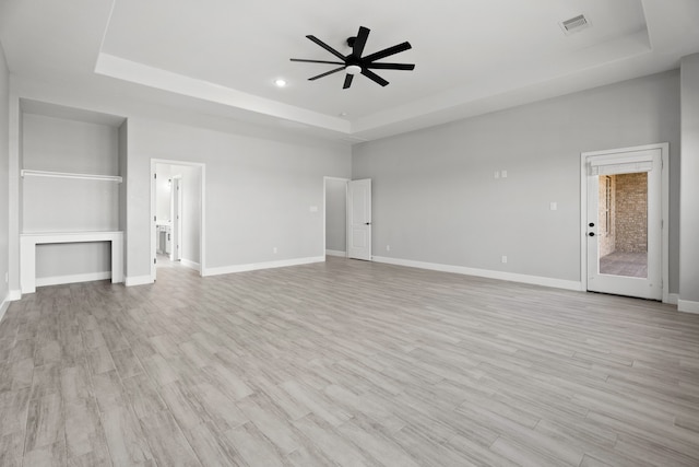 unfurnished living room with light hardwood / wood-style flooring, a tray ceiling, and ceiling fan