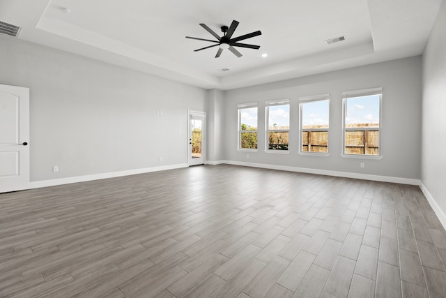 spare room featuring a tray ceiling, light wood-type flooring, and ceiling fan