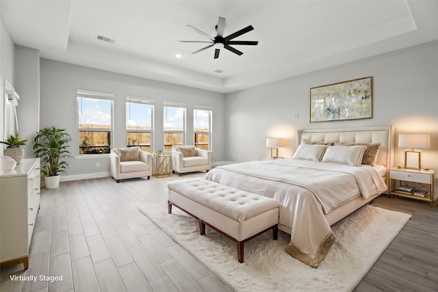 bedroom with hardwood / wood-style floors, a tray ceiling, and ceiling fan