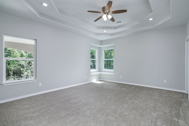 empty room featuring a tray ceiling, ceiling fan, and carpet floors