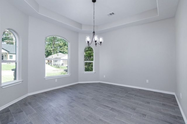 spare room with an inviting chandelier, a tray ceiling, and dark hardwood / wood-style floors