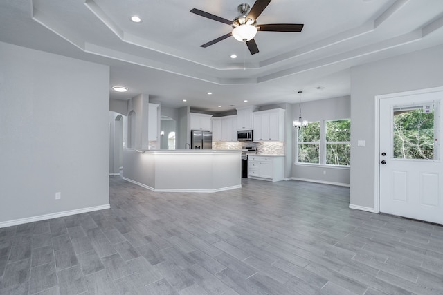 unfurnished living room with ceiling fan with notable chandelier, a raised ceiling, and light hardwood / wood-style flooring