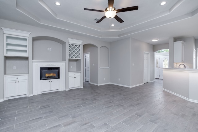 unfurnished living room featuring ceiling fan, a tray ceiling, a high end fireplace, and light hardwood / wood-style flooring