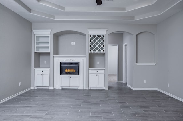 unfurnished living room featuring wood-type flooring, a high end fireplace, ceiling fan, and a tray ceiling