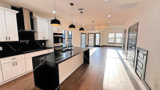 kitchen featuring a center island with sink, wall chimney exhaust hood, dark wood-type flooring, and sink