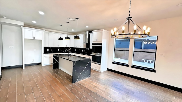 kitchen featuring dark hardwood / wood-style floors, an island with sink, white cabinetry, hanging light fixtures, and decorative backsplash