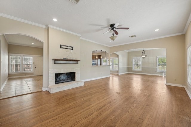 unfurnished living room featuring ceiling fan with notable chandelier, crown molding, hardwood / wood-style floors, and a brick fireplace