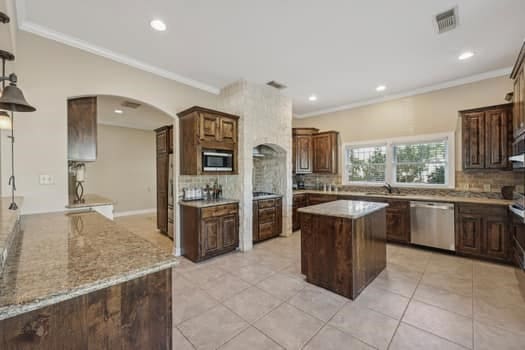 kitchen with light stone countertops, appliances with stainless steel finishes, tasteful backsplash, and a kitchen island