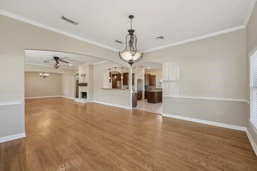 unfurnished living room with ceiling fan with notable chandelier, wood-type flooring, and crown molding