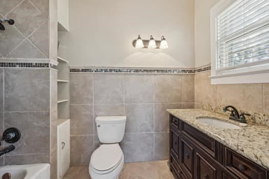 full bathroom with tile walls, vanity, toilet, and tile patterned floors