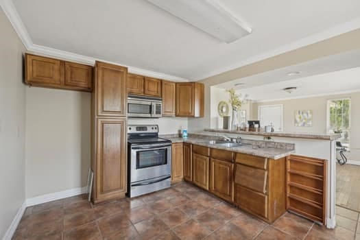 kitchen featuring ornamental molding, kitchen peninsula, appliances with stainless steel finishes, and dark tile patterned floors