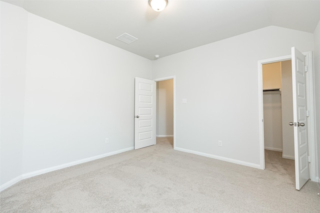 unfurnished bedroom featuring vaulted ceiling, a walk in closet, light carpet, and a closet